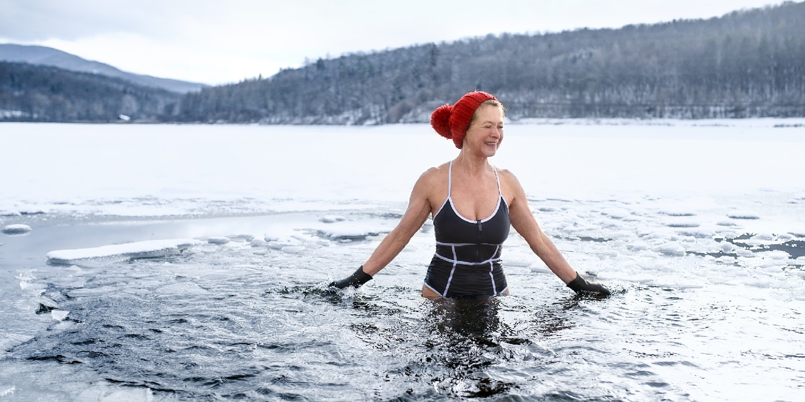 Front view of active senior woman in swimsuit outdoors in water in winter, cold therapy concept