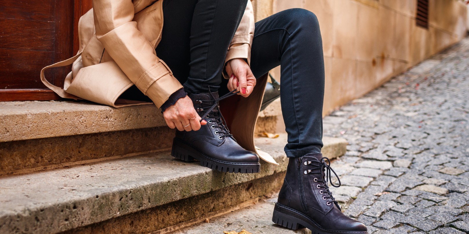 Stylish woman tying shoelace of black ankle boot