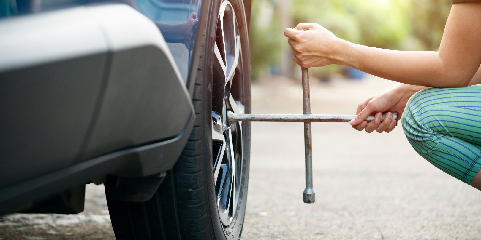 Woman driver with tyre iron changing wheel on a roadside