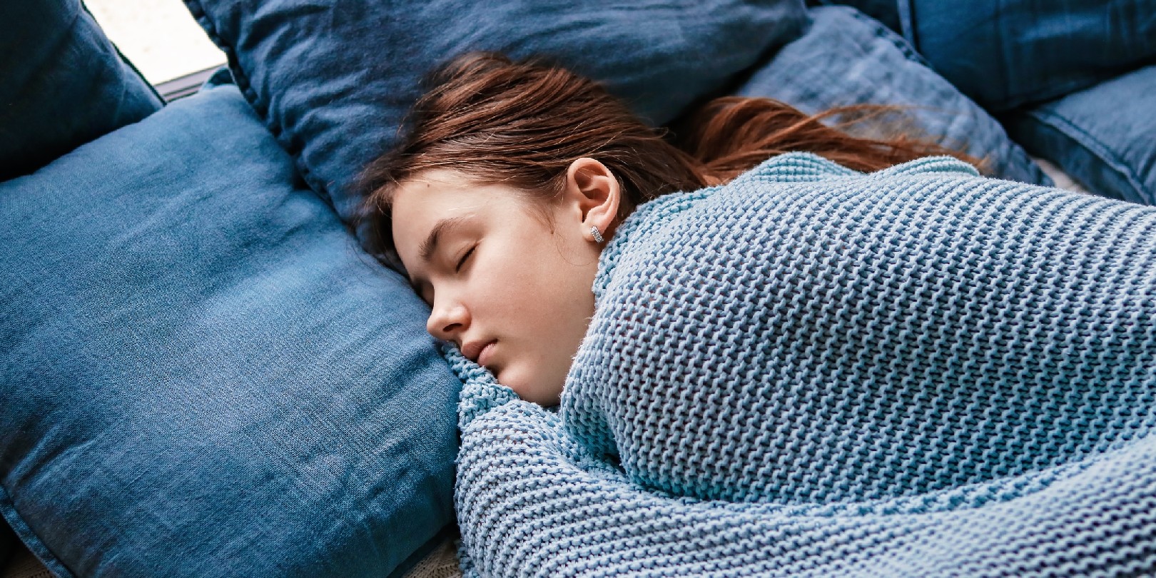 Young teenager girl sleeping snuggled in warm knitted blue blanket