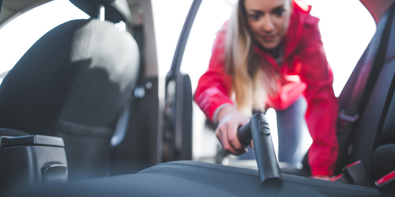 Young woman is cleaning car with vacuum cleaner