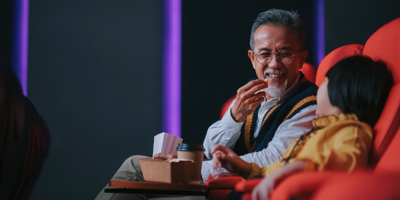 Asian chinese active senior man and his granddaughter enjoy watching movie in cinema movie theatre