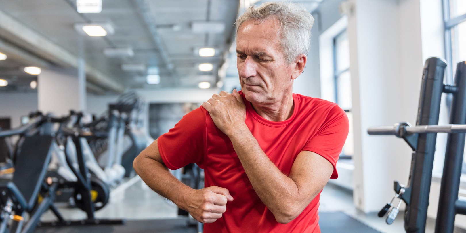 Mature man feeling pain in his shoulder during workout at rehabilitation center.