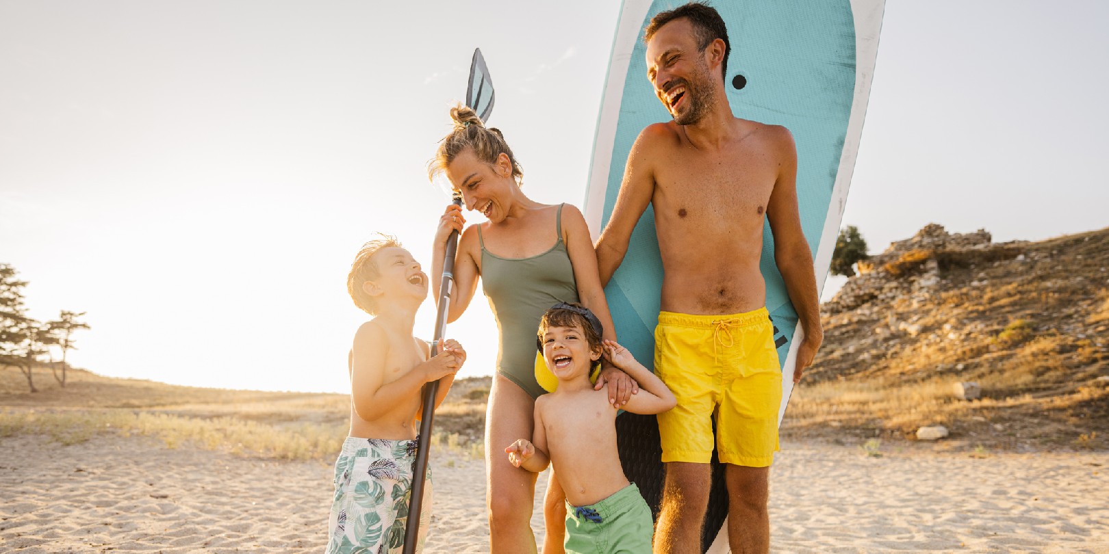 Photo of a smiling family at the beach, ready for paddleboarding