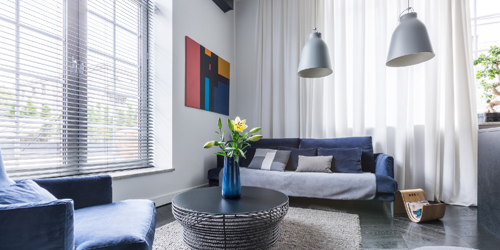 Living room with blue upholstered furniture, window blinds and white net curtain