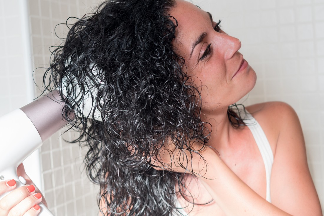 Young woman drying her hair with diffuser